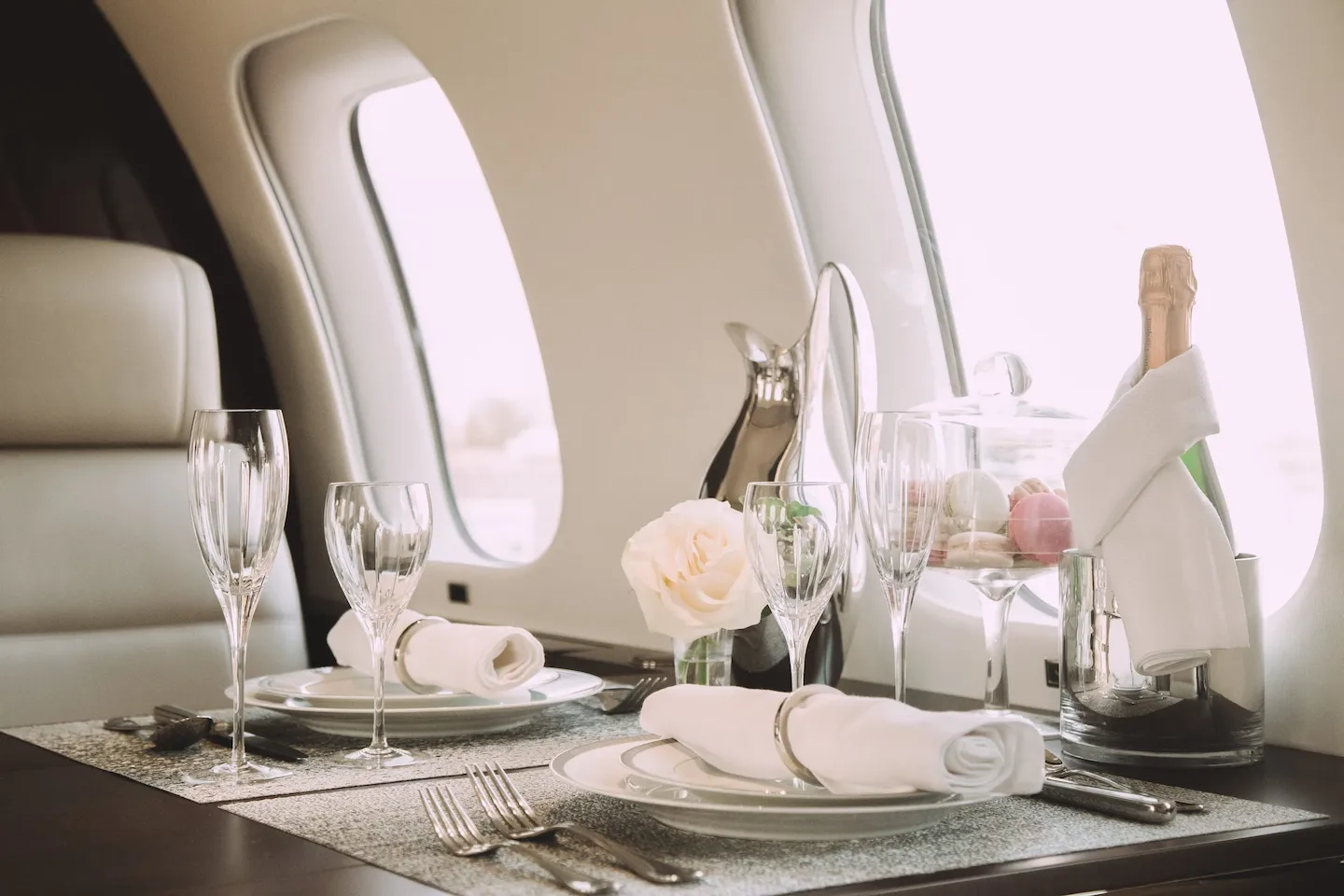 A full dining set up on a table inside of a private jet, featuring a bottle of champagne.