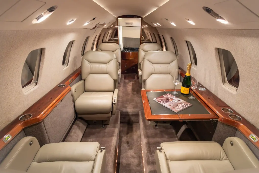 Interior of a Cessna private jet. On the tray table there is a magazine and a bottle of champagne.